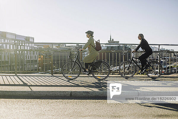 Seitenansicht von weiblichen Geschäftsleuten  die an einem sonnigen Tag mit dem Fahrrad auf der Fahrbahn fahren