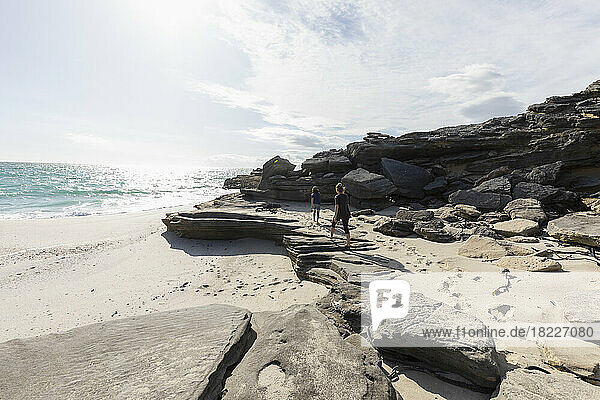 South Africa  Gansbaai  Teenage girl (16-17) with younger brother (8-9) walking on rocks on beach