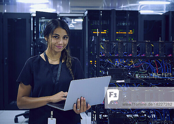 Portrait of smiling female technician using laptop in server room