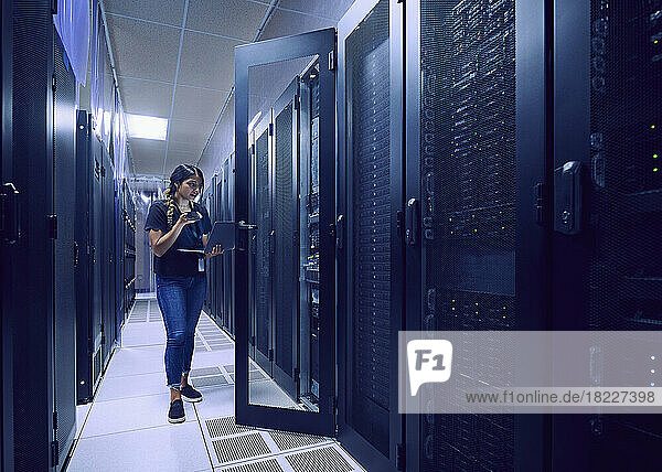 Female technician using smart phone and laptop in server room