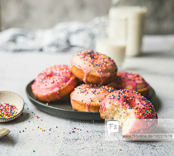 Plate of vanilla cake donuts with pink icing and sprinkles.