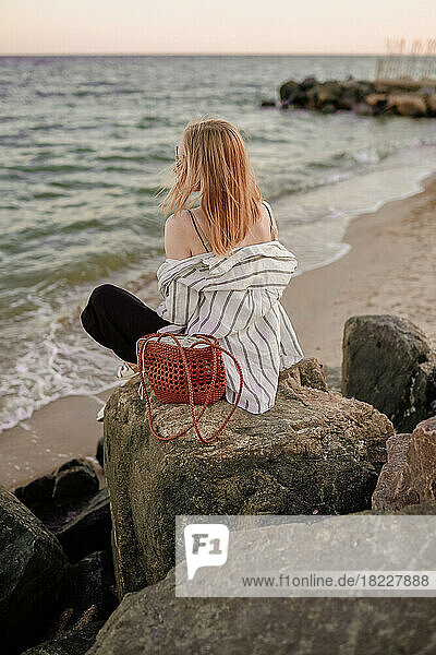 The girl sits on the rocks and looks at the sea or the ocean.