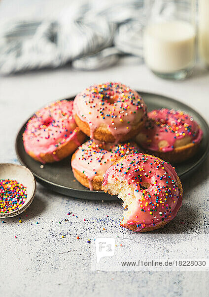 Plate of yummy vanilla cake donuts with pink icing and sprinkles.