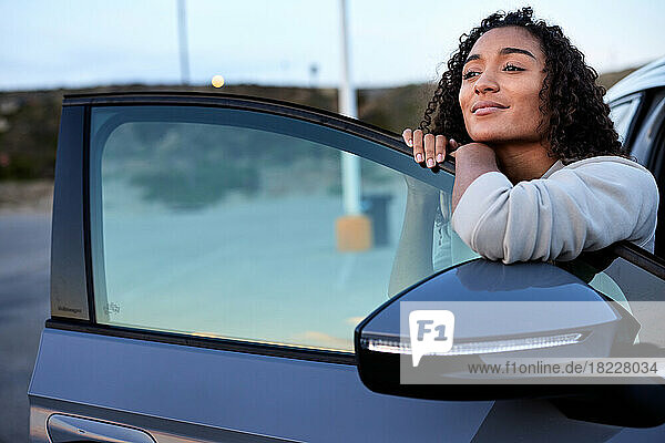 Smiling woman day dreaming while leaning on vehicle door