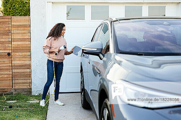 Woman holding charging cable while standing by electric car