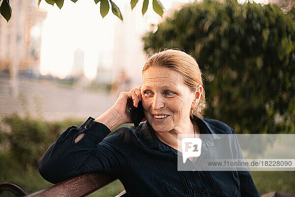 Happy mature business woman talking on mobile phone sitting in city