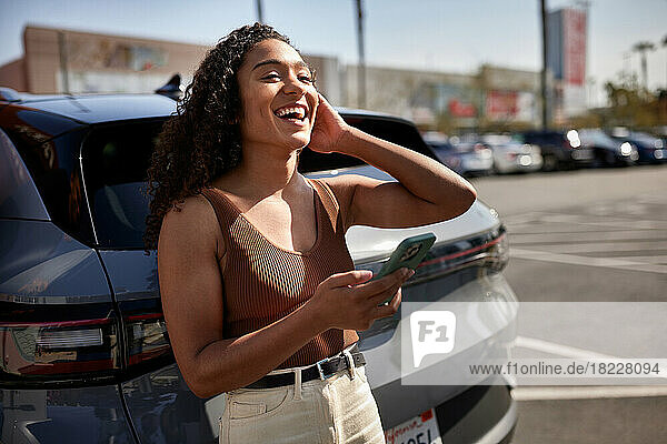 Woman with smart phone laughing in parking lot on sunny day