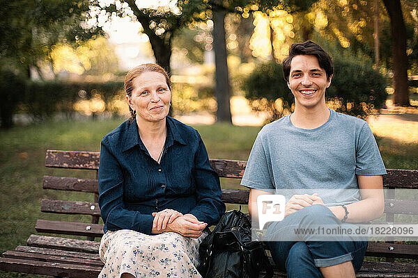 Happy mature mother and smiling adult son sitting on the bench in park