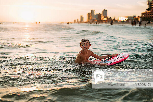 Young boy at sunset swimming in the ocean with cityscape background