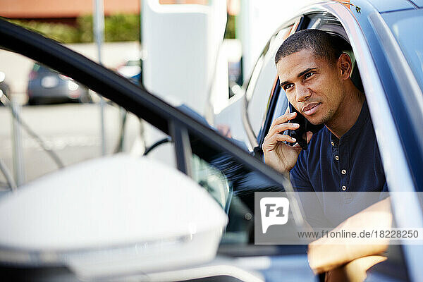 Mid adult man talking on smart phone sitting in electric car