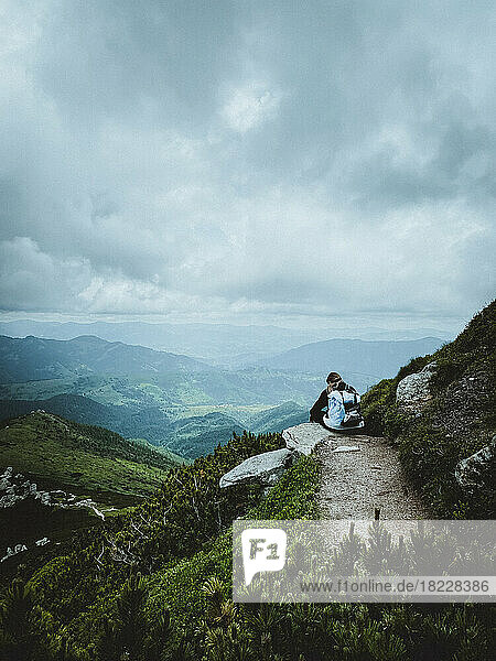Female tourist sit on cliff's edge during mountain hiking
