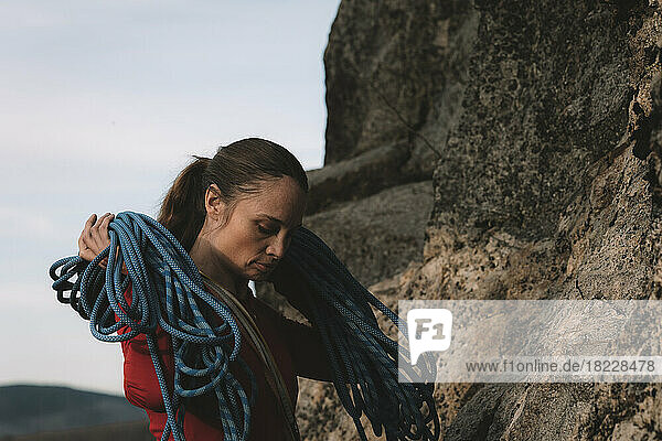 A woman in a red shirt holding a rope to rock climbing on a sunny day.