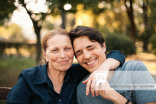 Happy mature mother hugging smiling adult son in park in summer