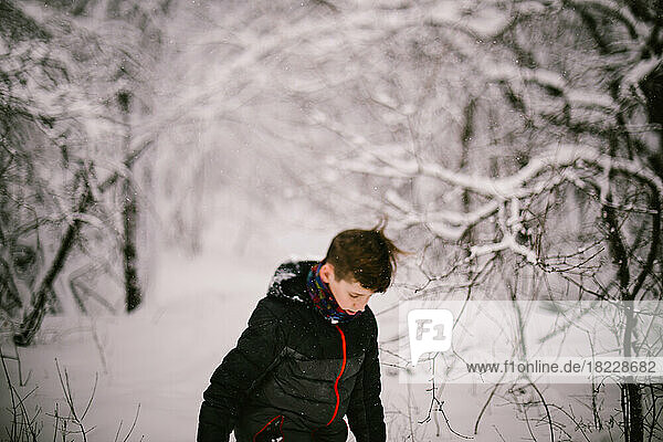 Boy in ski coat plays in white snow covered forest