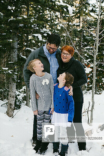 Family laughs and hugs in sweaters in snowy forest