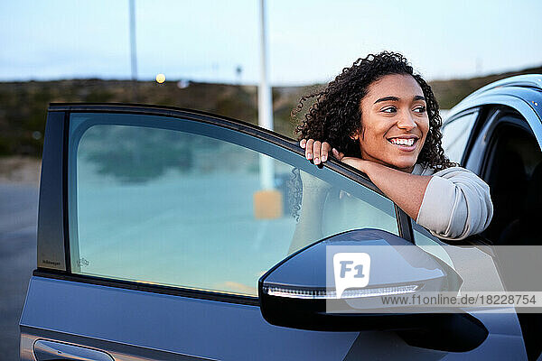 Happy woman looking away while leaning on car door