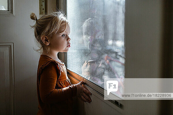 Young girl looking out from inside at the front door