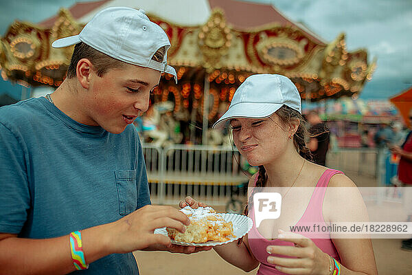 Two happy teens sharing a funnel cake at a fair