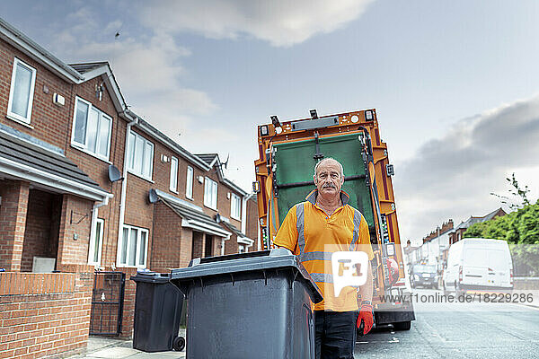 Portrait of refuse collector with bin and refuse truck