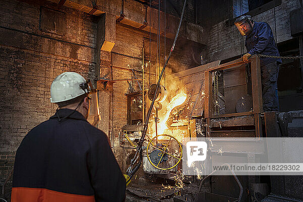 Workers pouring molten iron from furnace in iron foundry