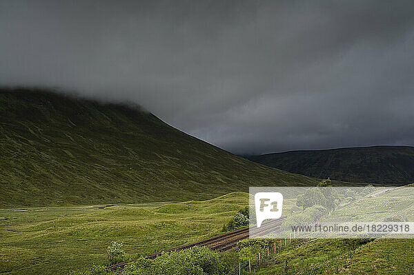 UK  Scotland  Storm clouds above green landscape with railroad tracks