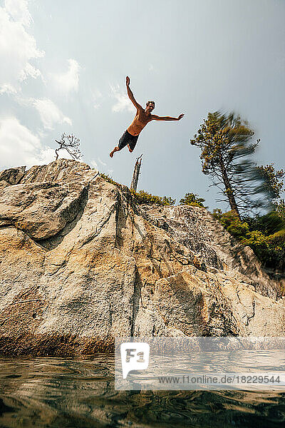 Man jumping from cliff into lake