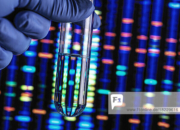 Hand holding test tube with illuminated genetic data in background
