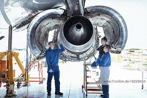 Apprentice aircraft maintenance engineers work underneath large jet engine