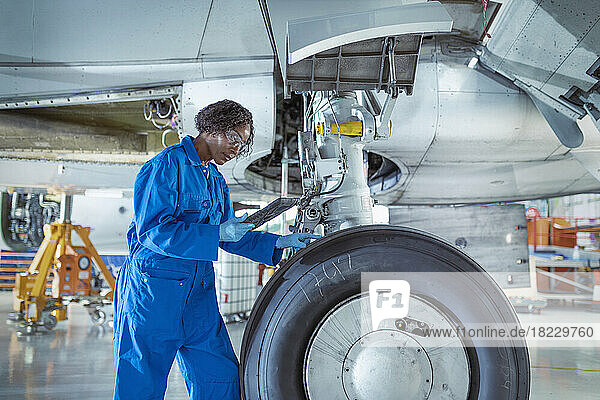 Female aircraft maintenance engineer underneath jet with digital tablet