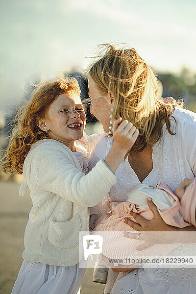 Happy girl embracing and having fun with daughter on sunny day