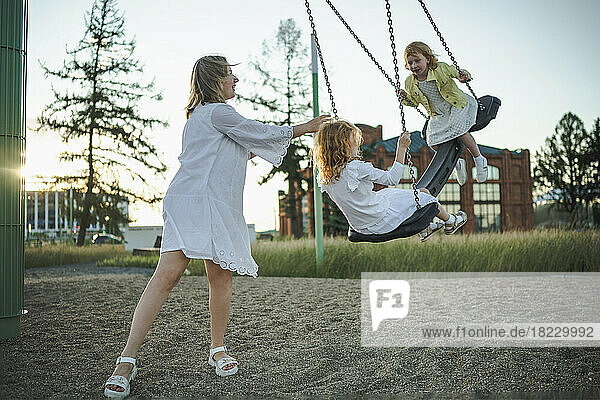 Glückliche Mutter genießt es mit ihren Töchtern  die im Park auf der Schaukel schaukeln