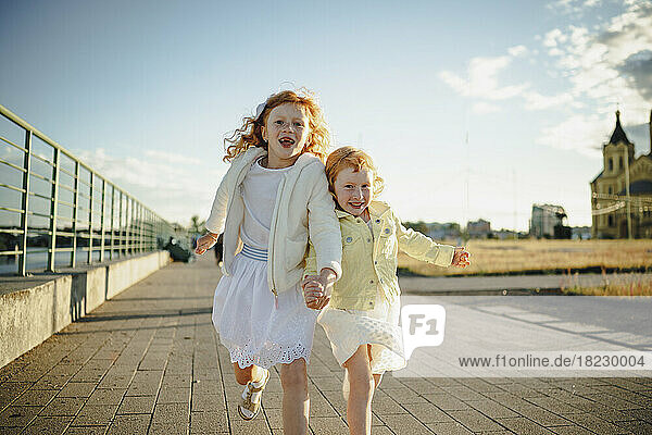 Happy girls holding hands and running on footpath