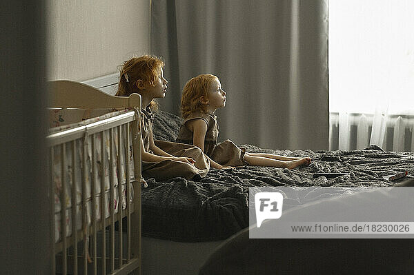 Girl with sister sitting on bed watching TV at home