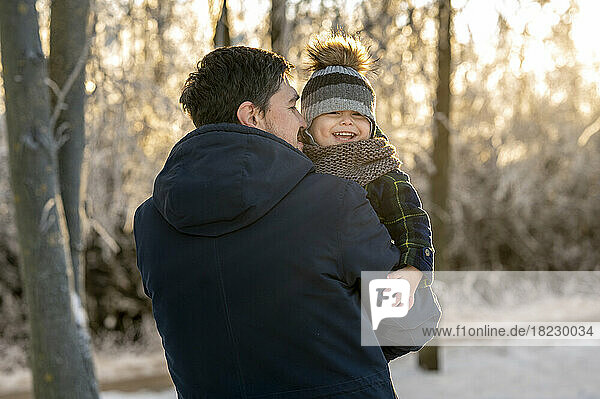 Smiling man carrying happy son in winter park