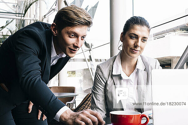 Smiling businesswoman with colleague using laptop at table in cafe