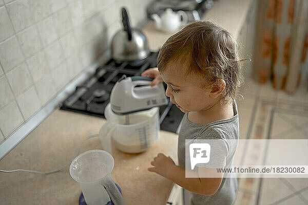 Toddler mixing batter with electric mixer in kitchen at home