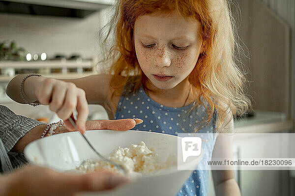 Redhead girl mixing cheese in bowl at home
