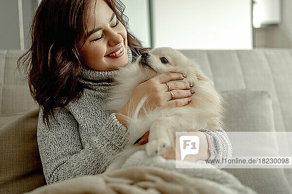 Cheerful young woman stroking Pomeranian dog at home