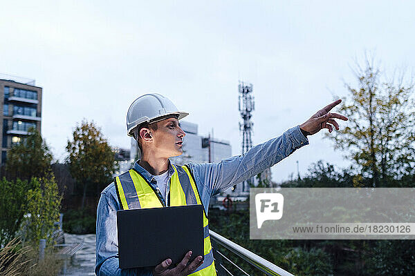 Young engineer gesturing holding laptop at dusk