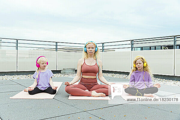 Mother and daughter with headphones meditating on rooftop