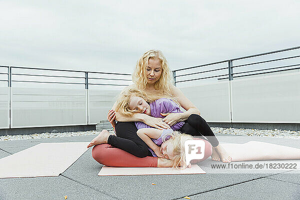 Mother embracing daughters on rooftop under sky