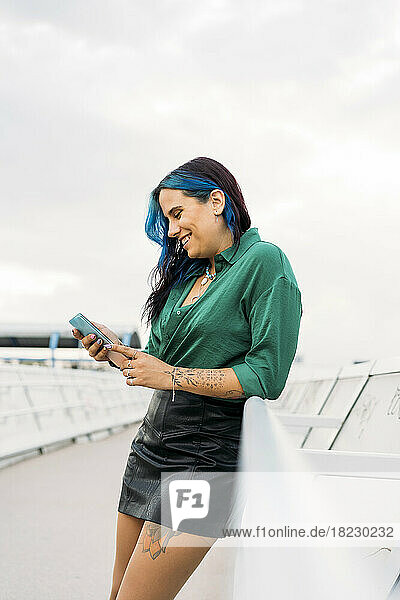 Smiling woman using smart phone leaning by railing