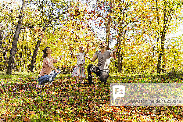 Playful parents with daughter throwing autumn leaves n park