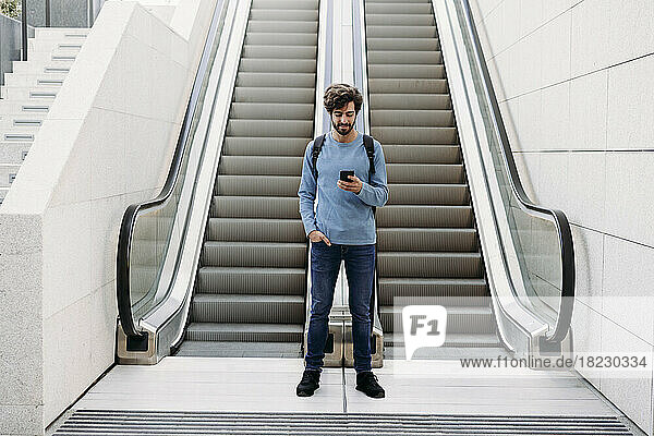 Young man using smart phone standing in front of escalator