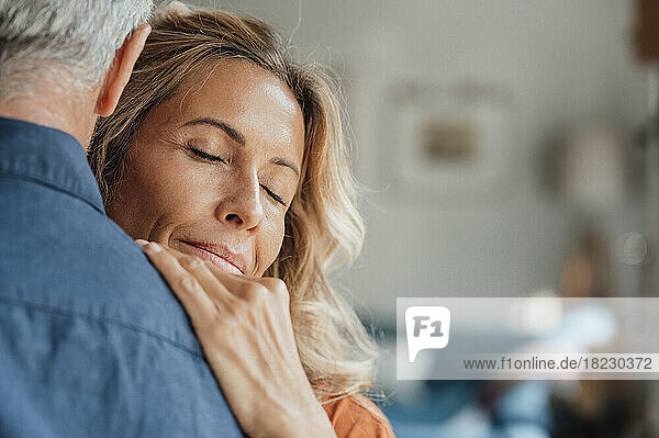 Reife Frau mit geschlossenen Augen umarmt Mann zu Hause