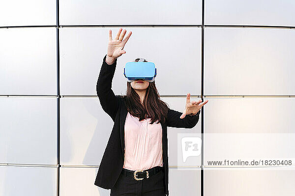 Young woman wearing virtual reality simulator gesturing in front of wall