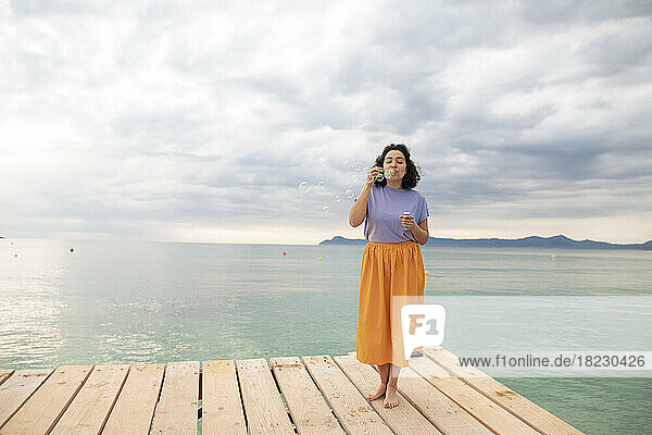 Frau steht auf einem Steg und bläst Seifenblasen vor dem Meer