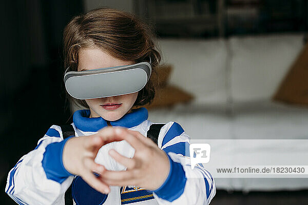 Girl in space costume wearing virtual reality simulator gesturing at home