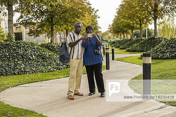 Mann und Frau nutzen Smartphone und stehen auf Fußweg im Park