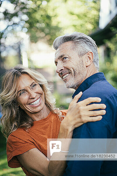 Cheerful mature man and woman embracing and having fun together in back yard